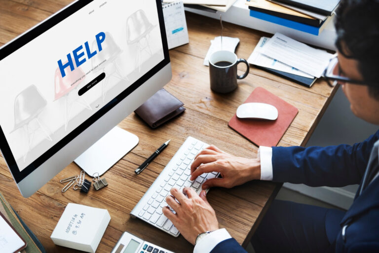 Mężczyzna w garniturze pracujący przy komputerze w biurze, ekran z napisem "HELP"